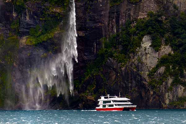 Southern Discoveries cruise travelling beneath waterfalls in Milford Sound